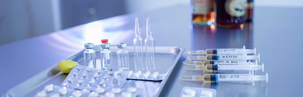 На столе лежат таблетки, шприцы и бутылки алкоголя